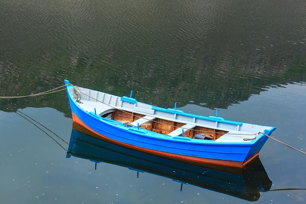 Barco en la superficie del agua del lago y reflejos suyos y de montaña.