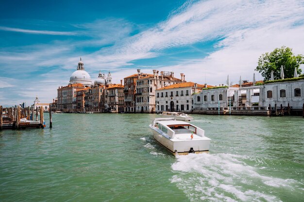 Barco turístico del Gran Canal con la basílica de Santa Maria della Salute contra el cielo azul y las nubes blancas