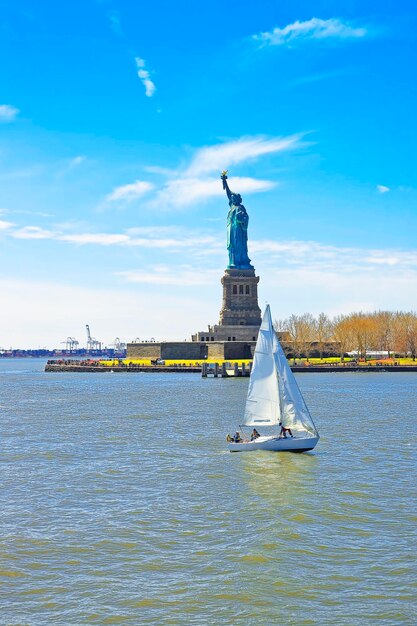 Barco de vela y estatua de Liberty Island, New York City, los E.E.U.U. Bahía superior de Nueva York. Los turistas están en la isla y en el barco.