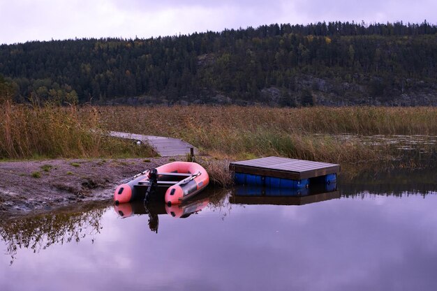 Foto barco vermelho de borracha perto do cais no lago no fundo das montanhas