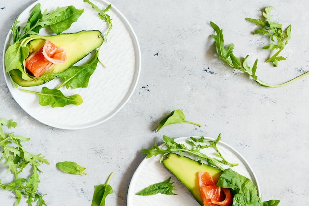 Barcos de aguacate maduro con rodajas de trucha salada, salmón y verduras frescas sobre un fondo gris. Botes de aguacate rellenos de salmón con limón, hojas de espinaca y rúcula, concepto de comida sana, dieta.