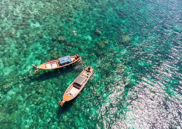 Barcos de cola larga de madera en el mar esmeralda con arrecifes de coral en el agua