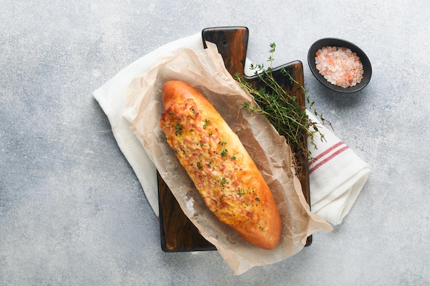 Barcos de baguete Sanduíche assado quente no pão baguete com presunto, bacon, legumes e queijo em pergaminho e suporte de madeira em fundo cinza de concreto Vista superior Copiar espaço