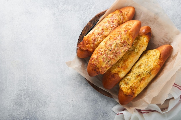 Barcos de baguete Sanduíche assado quente no pão baguete com presunto, bacon, legumes e queijo em pergaminho e suporte de madeira em fundo cinza de concreto Vista superior Copiar espaço