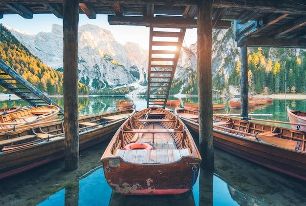 Barcos de madeira sob a casa no famoso lago Braies ao nascer do sol no outono nas Dolomitas Itália Paisagem com escadas montanhas água azul árvores coloridas no outono no amanhecer Viagens na Europa Alpes