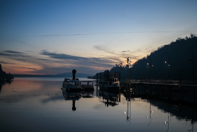 Barcos de pesca atracados em um pequeno cais de madeira cercado por montanhas durante o pôr do sol no Chile