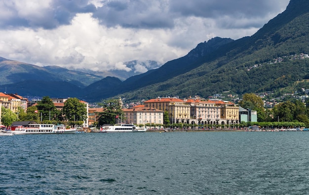 Barcos en el paseo marítimo del lujoso resort en Lugano en el lago Lugano y las montañas de los Alpes en el cantón de Ticino, Suiza.