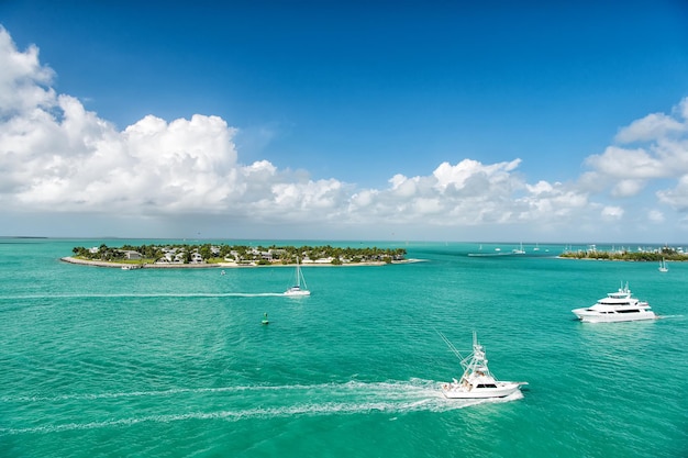 Barcos turísticos de crucero o yates flotando en la isla con casas y árboles verdes en aguas turquesas y cielo azul nublado, yates y vida isleña alrededor de la hermosa Key West Florida, EE.UU.