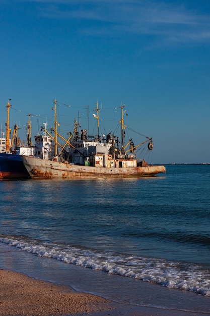 Barcos viejos en el muelle en el mar con una playa vacía con un cielo azul claro Puerto marítimo desierto en la costa grúas y barcos