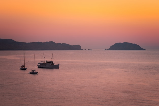 Barcos viendo la puesta de sol en agosto en la playa de Cavalleria en la costa norte de Menorca, España.