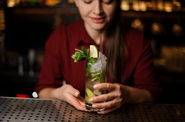 Bardame steht an der Bar und hält einen fertigen Mojito in der Hand