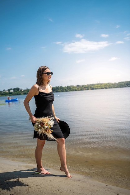 Barfüßige Frau geht im Sommertag im schwarzen Kleid im Teich spazieren