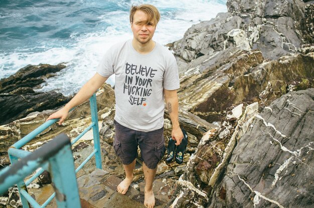 Barfuß junger Mann am Meer, der auf Steinstufen steht