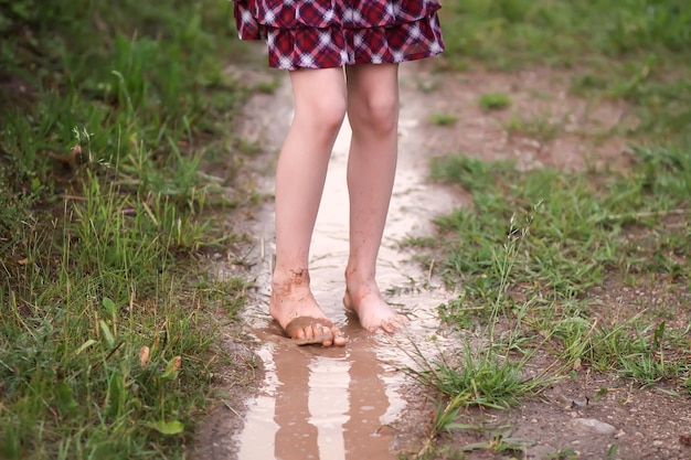 Barfußmädchen geht nach dem Sommerregen auf dem Land durch eine Wasserpfütze.