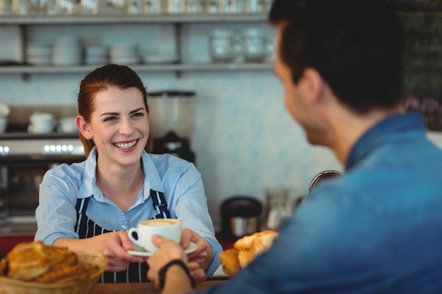 Barista alegre dando café al cliente en la cafetería.