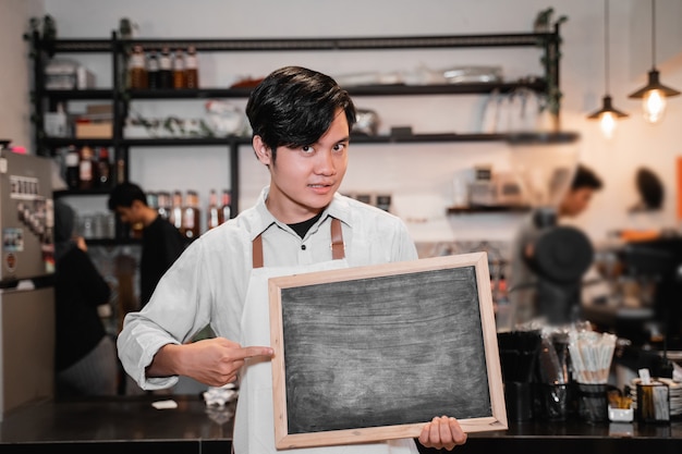 Barista asiático segurando e apontando uma placa em frente ao bar