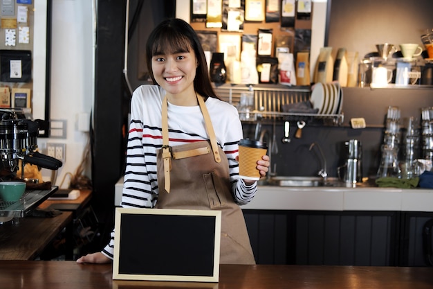 Barista asiático sonriente que sostiene la taza de café en el contador en cafetería