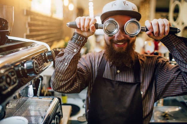 Barista barbudo en delantal con cezve y tapa los ojos con ellos