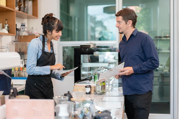 Barista-Besitzerin in Schürze lächelt und benutzt Tablet-Bestellungen beim Kunden im Café