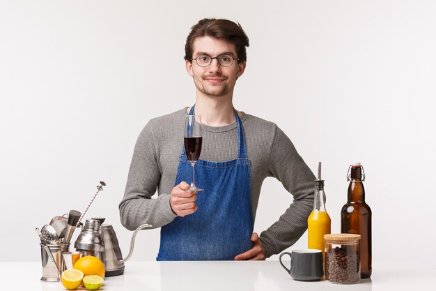 Barista, Cafe Worker und Barkeeper-Konzept. Porträt des erfreuten glücklichen erfolgreichen männlichen Unternehmers des Kleinunternehmens erfreut nach dem Schließen des Geschäfts, der Glas Wein einschenkt und zufrieden lächelt