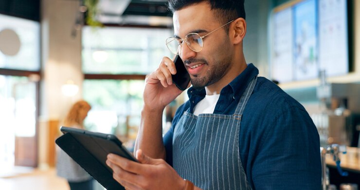 Foto barista chamada telefônica e tablet para comunicação de restaurante gerenciamento on-line ou serviço ao cliente em café proprietário de pequena empresa garçom ou homem em móvel e inventário digital para startup de cafeteria