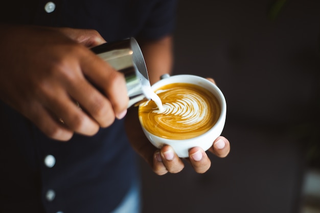 Barista, das eine Tasse Kaffee Lattekunst in der Kaffeestube macht.