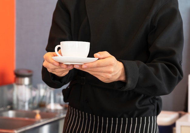 Barista de avental preto segurando e servindo uma xícara de café quente