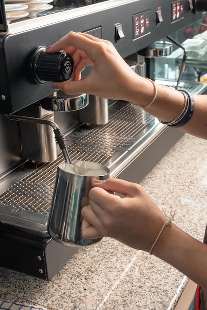 Barista de mulher fechada em avental preparando e derramando leite em xícara quente na cafeteria