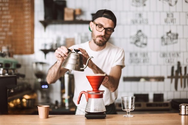 Barista de óculos e boné em pé no balcão e preparando o café enquanto trabalhava no café