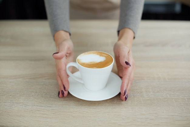 Barista en delantal en cafetería da café recién preparado al cliente