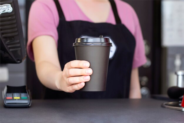 Barista en un delantal tiene café caliente en un vaso de papel