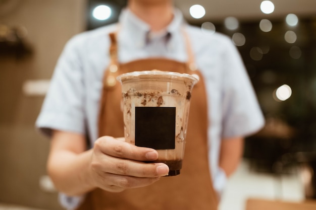 Barista, der ein Glas Mitnehmerkaffee in der Plastikschale gibt.