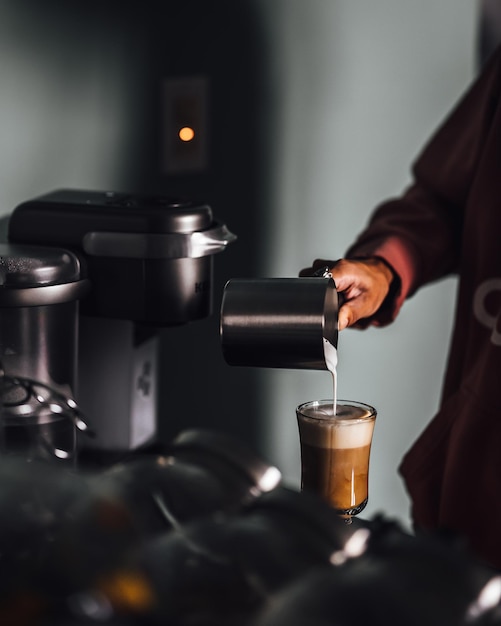 Barista, der einer Tasse Kaffee in einem Café gedämpfte Milch hinzufügt