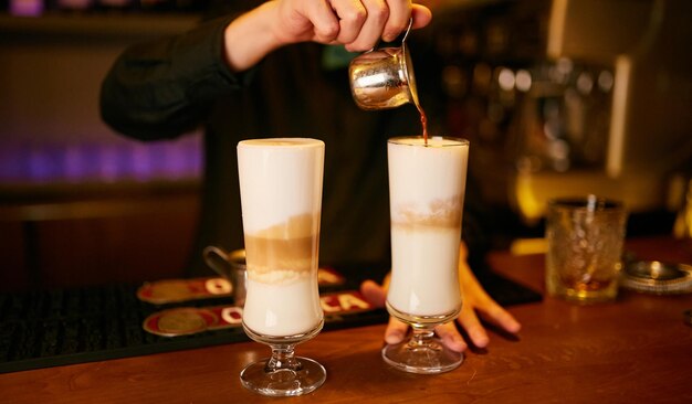 barista derrama café em um cappuccino em um copo de vidro em um balcão de bar