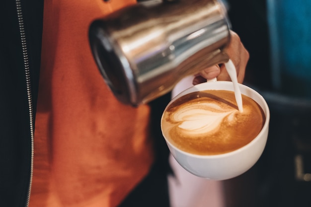 Barista derramando leite na xícara de café fazendo coração