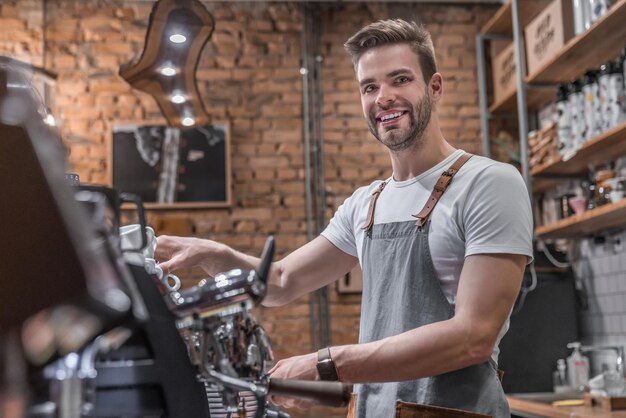 Barista des jungen Mannes, der eine Tasse Kaffee in der Cafeteria kocht