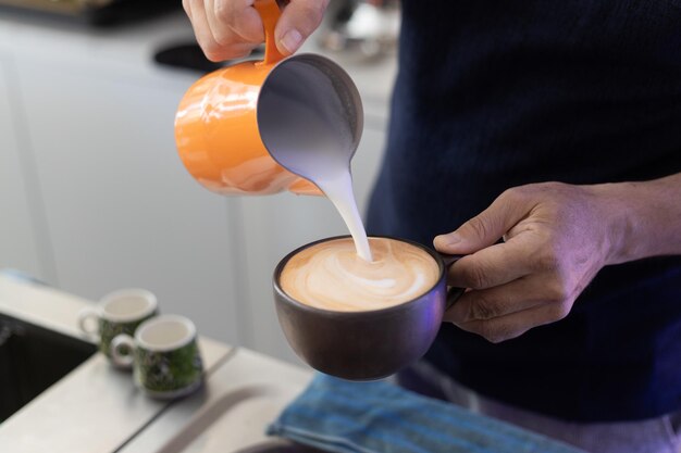 Foto barista em um café fazendo arte de latte com leite e café de perto a mão do barista derramando leite fazendo arte de latte