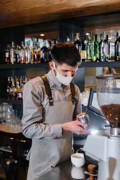 Un barista enmascarado prepara un delicioso café en el bar de una cafetería. El trabajo de los restaurantes y cafés durante la pandemia.