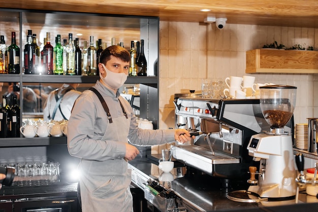 Un barista enmascarado prepara un exquisito café delicioso en la barra de una cafetería El trabajo de los restaurantes y cafeterías durante la pandemia