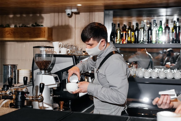 Un barista enmascarado prepara un exquisito café delicioso en la barra de una cafetería El trabajo de los restaurantes y cafeterías durante la pandemia