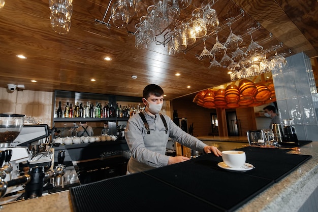 Un barista enmascarado sirve exquisitamente café preparado en una cafetería moderna durante una pandemia Sirviendo café preparado a un cliente en una cafetería