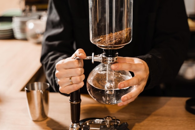 Barista está segurando o sifão antes de começar a ferver a água dentro do sifão Processo de fabricação de café com sifão no café