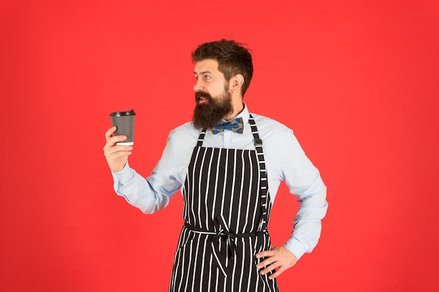 Barista experiente. fundo vermelho do homem maduro. servo habilidoso. avental do chef barista hipster. barman elegante e confiante. café bebida masculina. homem barbudo segurar levar café. garçom brutal no café.