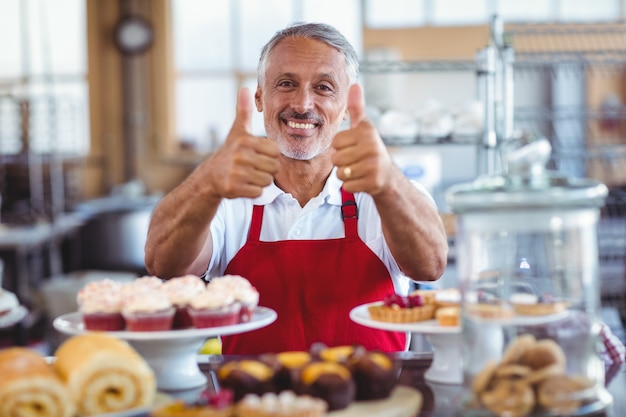 Barista feliz olhando câmera e gesticulando polegares para cima