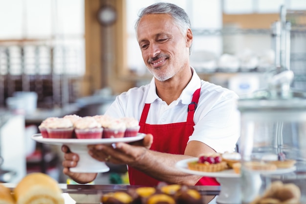 Foto barista feliz segurando um prato de cupcakes