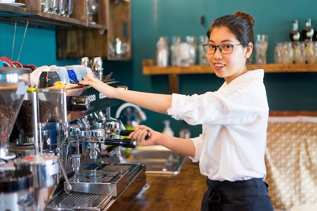 Barista fêmea alegre que prepara o café na cafetaria.