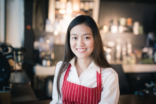 El barista femenino asiático lleva el delantal rojo que se coloca en un café