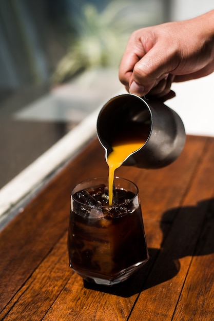 Barista gießt Milch in ein Glas Eiskaffee