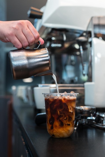 Barista gießt Milch in ein Glas Eiskaffee