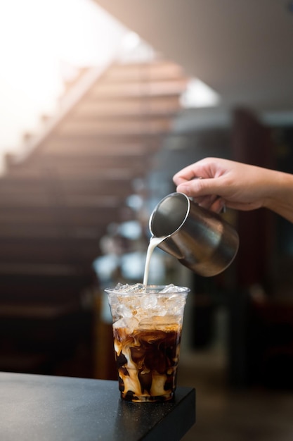 Barista gießt Milch in Eiskaffeeglas